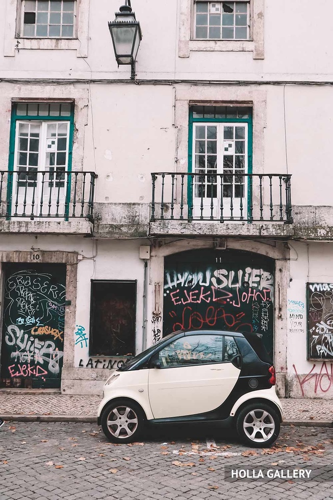 Белая машина у стены с граффити в Лиссабоне